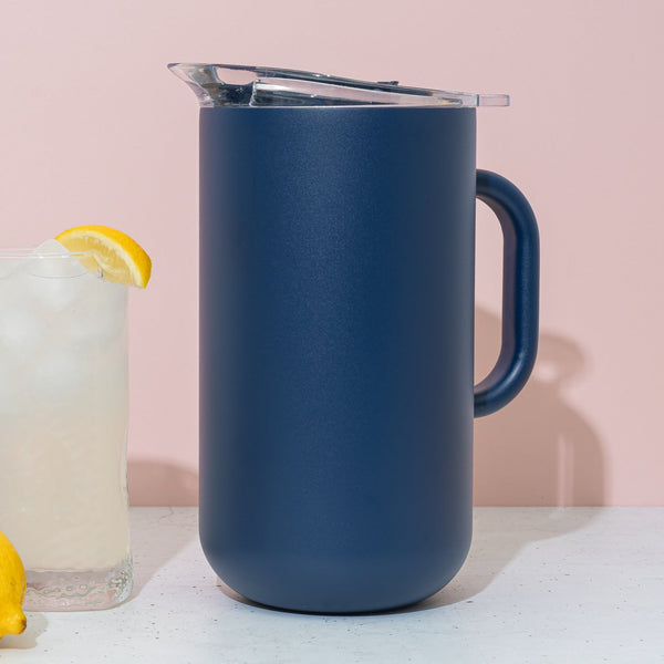 Blue pitcher with a glass of lemonade and lemons on a light pink background